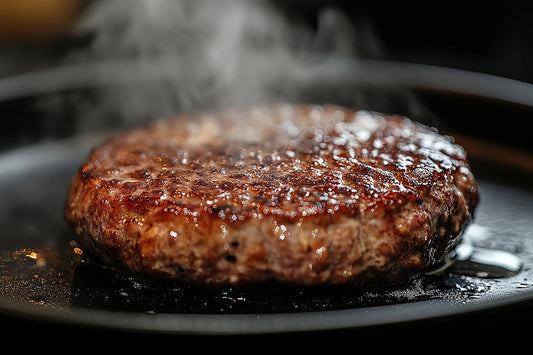 黒いフライパンの上で、表面に焼き色を付けながら湯気を上げるハンバーグの接写