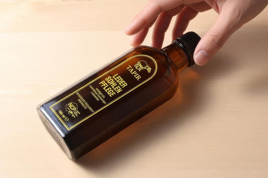 木の台に斜めに置かれたタピールのレザーソールオイルの茶色い瓶に手を添える様子