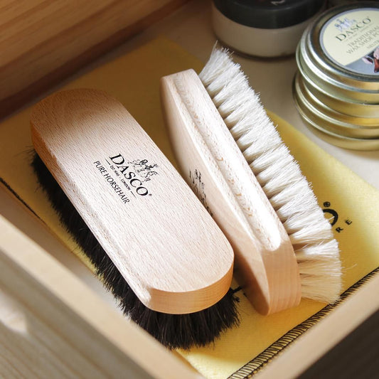 黄色いクロスと靴クリームの缶とともに道具箱に収めたダスコのホースヘアブラシ。黒毛と淡い毛の比較