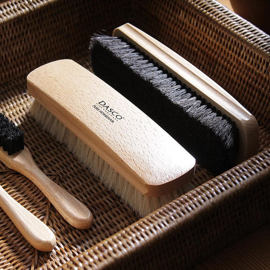 編みかごに並べたダスコのホースヘアブラシ ラージ。ロゴ入りの明るい木部と黒毛、淡い色の毛