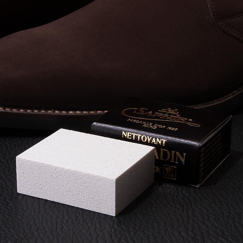 茶色の起毛革靴を背景に置いたサフィールノワールのラバークリーナー。白いブロックと黒い箱