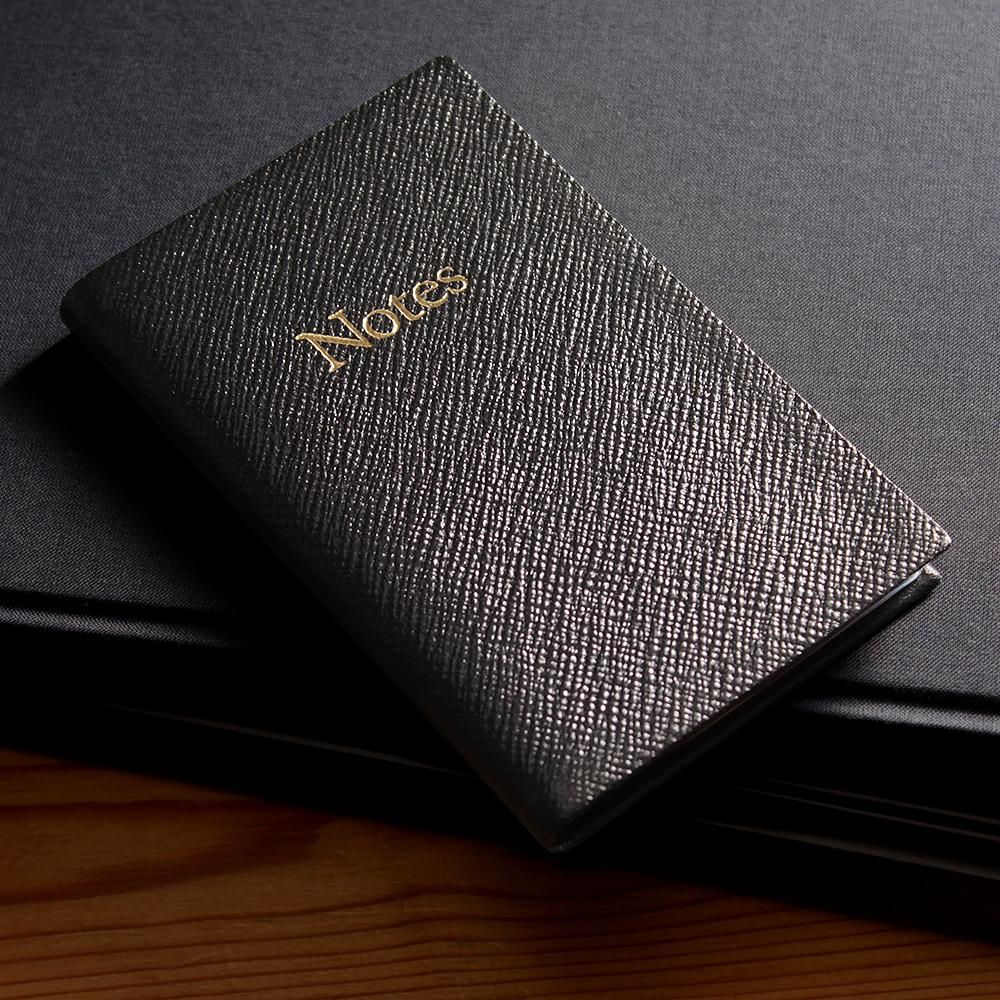 黒い布の上に置いたレザースミス オブ ロンドン NBB53Rノートブック。黒い表紙に金色のNotesの文字