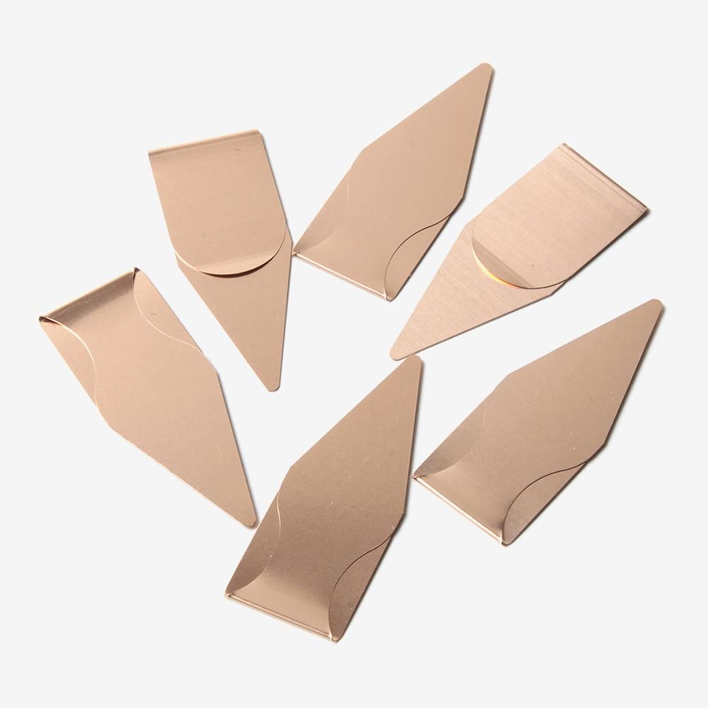 ブックダーツのブロンズ6個を白い背景に並べた拡大写真。細長い矢じり形と紙を挟む折り返し