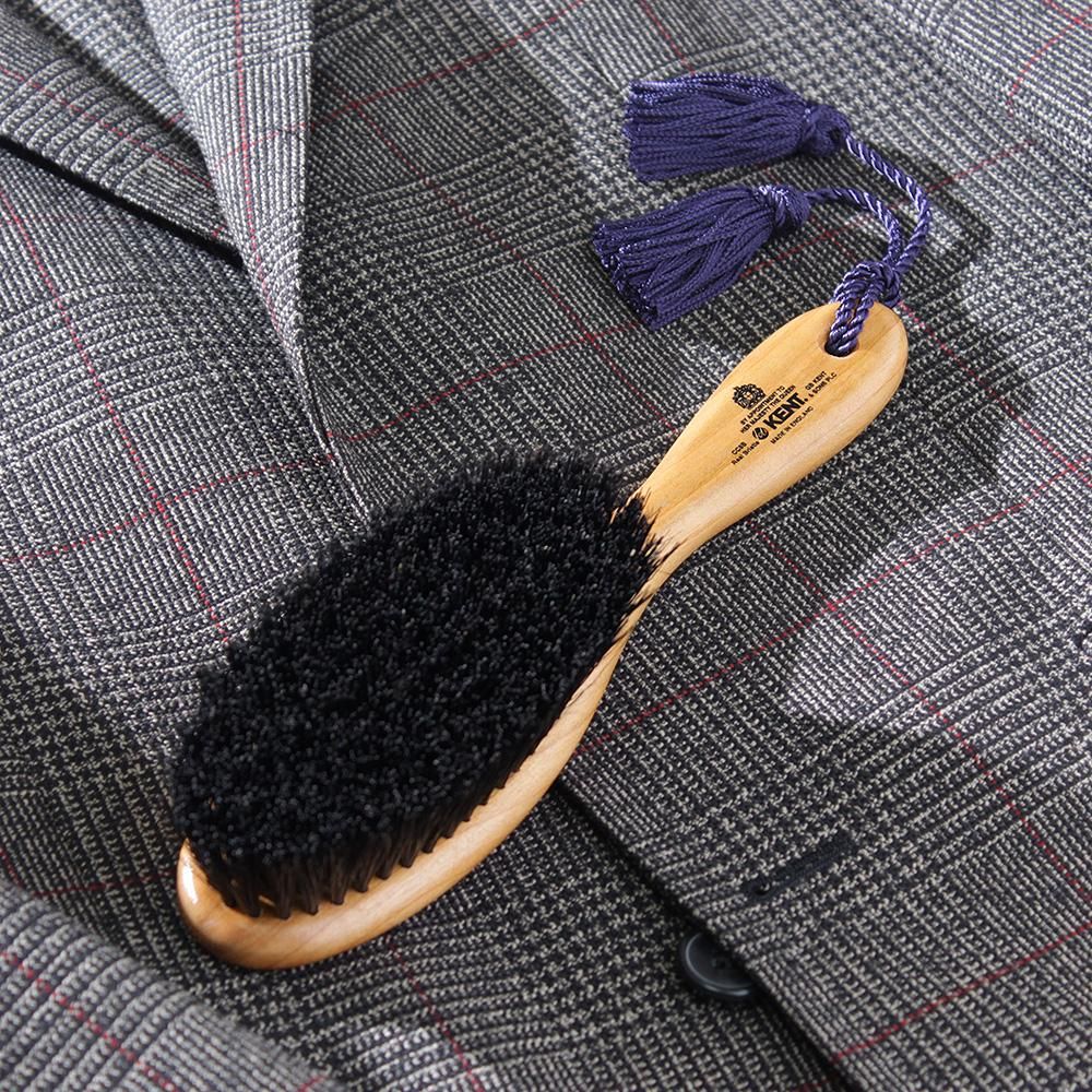ケントの洋服ブラシをグレーのチェック柄ジャケットに置いた写真。黒い毛束と紫のタッセル、木製ハンドル