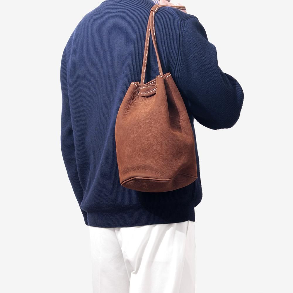 ESCALA巾着バッグのブラウンモデルを紺のニットと白いパンツに合わせて肩に掛けた使用例
