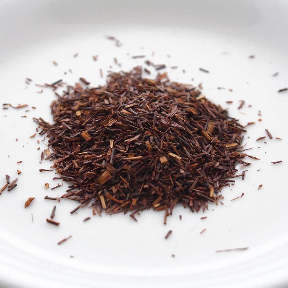 ルイボスティーの茶葉を白い皿に盛った拡大写真。赤茶色の細長い葉と茎