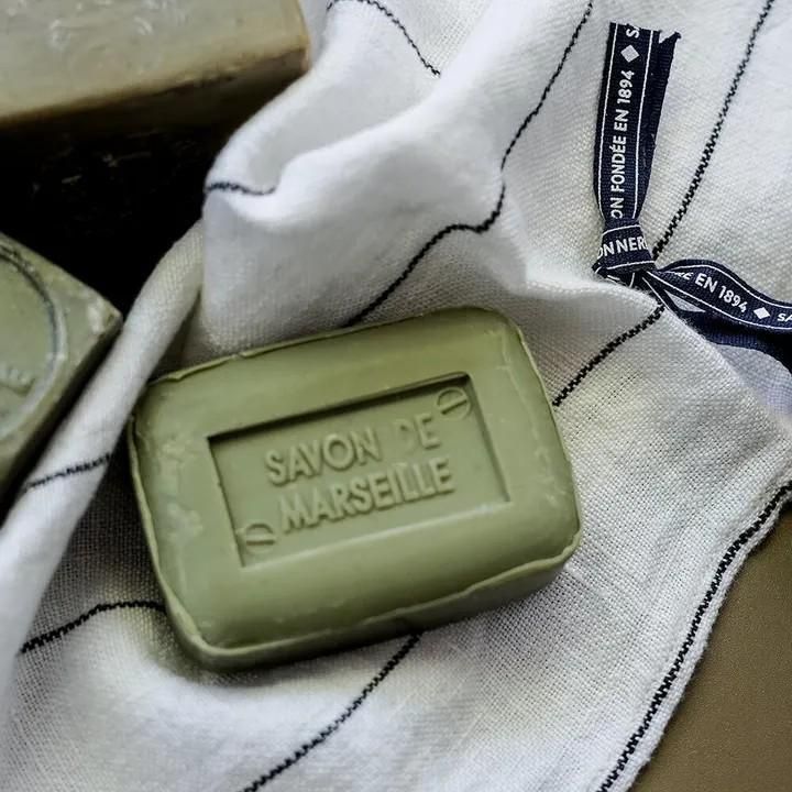 ラ コルベットのオリーブ石けん100g。縞模様の白い布の上に置いた緑色の長方形の本体