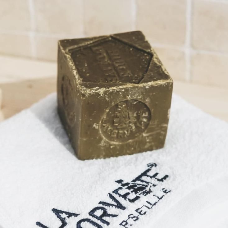 ラ コルベットのオリーブ石けん300g。ロゴ入りの白いタオルに置いた、刻印のある立方体の本体