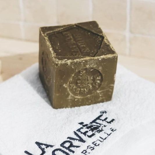 ラ コルベットのオリーブ石けん300g。ロゴ入りの白いタオルに置いた、刻印のある立方体の本体
