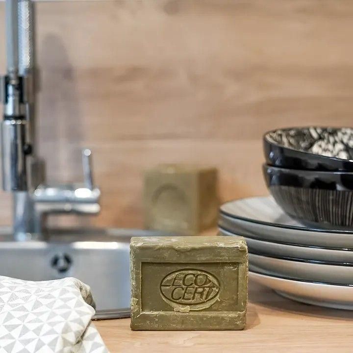 ECOCERTの刻印がある四角い食器用石けんを流し台の脇に置いた写真。隣に重ねた食器と白い布