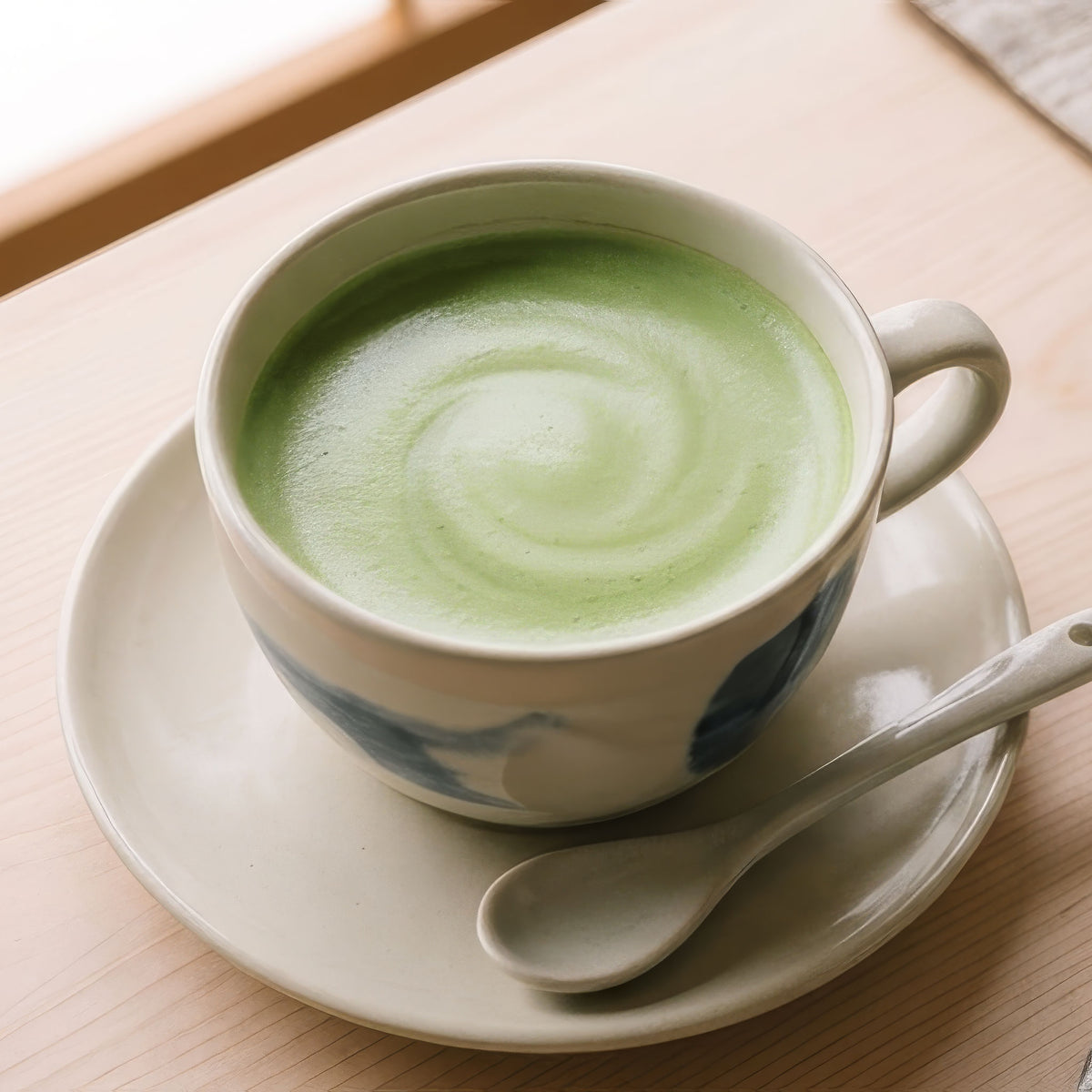カップとソーサーに注いだEECO抹茶ラテの出来上がり例。皿にスプーンを添えた様子